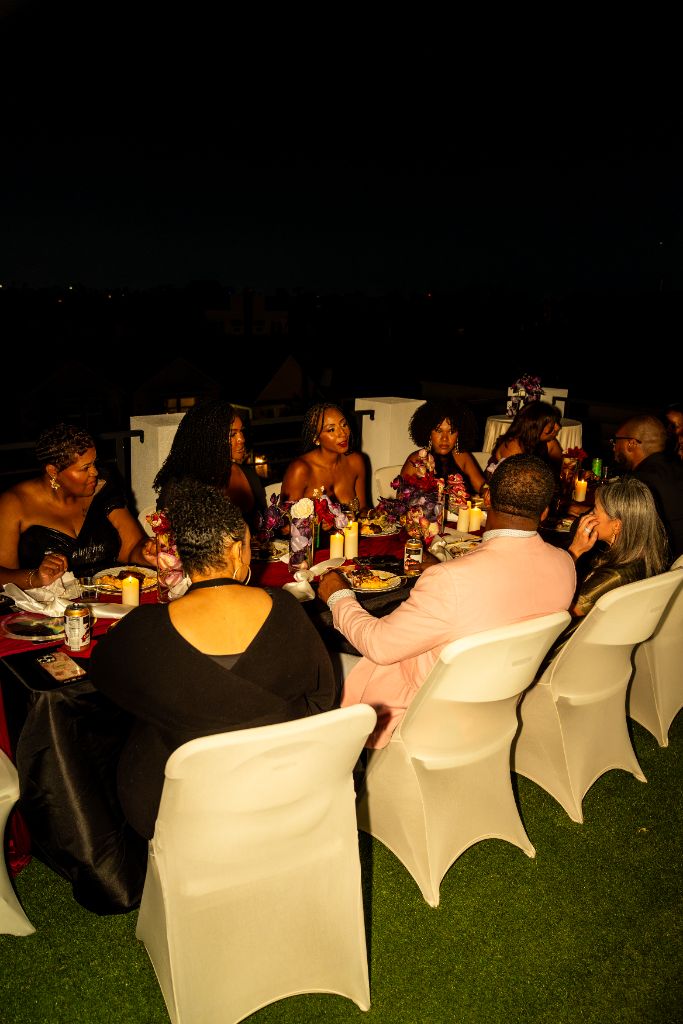Authentic photograph: Markesha and guests in genuine conversation around a candlelit rooftop dinner table at a real Rare Company gathering