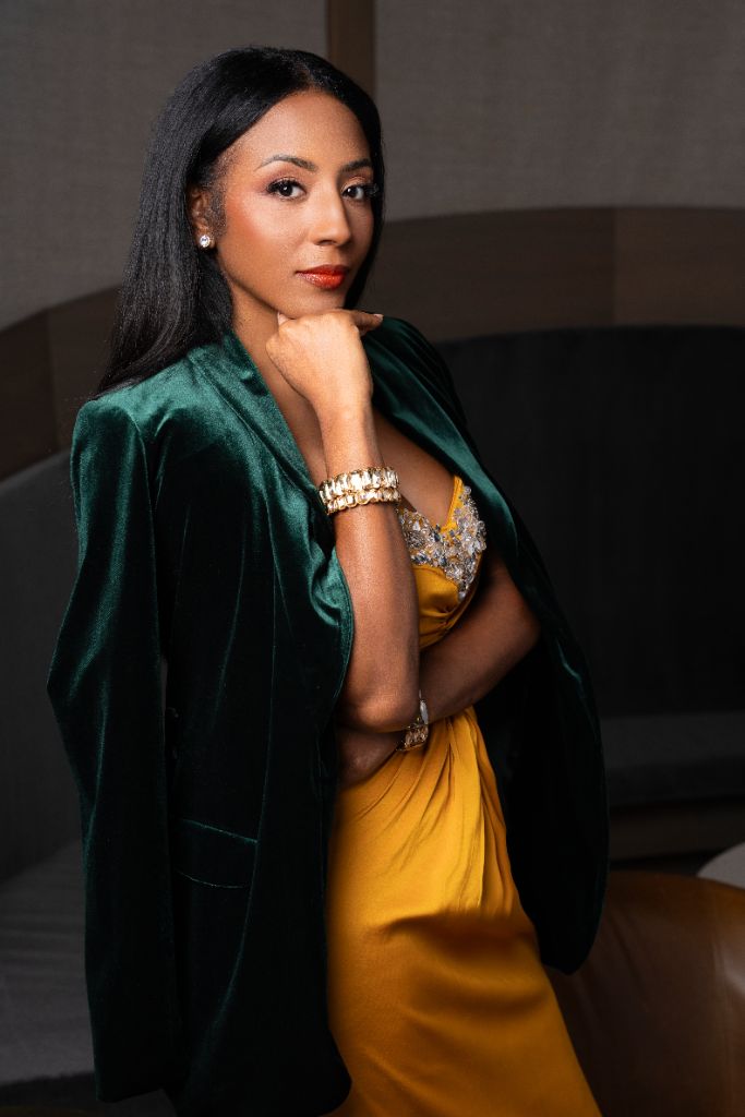 Markesha Kirkman in an emerald velvet blazer and gold gown, chin resting on her hand, direct gaze — authentic photograph